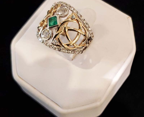 14k custom ring with Celtic design set with emerald centre with two round diamonds on each end with 1ct of diamonds surrounding centre